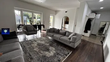 Geräumiges Wohnzimmer mit dunklem Holzboden, bequemen Sofas und Zugang zum Gartenbereich.