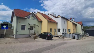 Reihenhäuser in verschiedenen Pastellfarben mit Satteldächern und kleinen Vorgärten von der Straße aus gesehen.