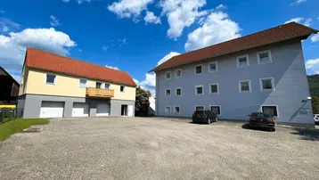 Zwei Gebäude mit rotem Satteldach und einem großen Schotterparkplatz unter blauem Himmel.