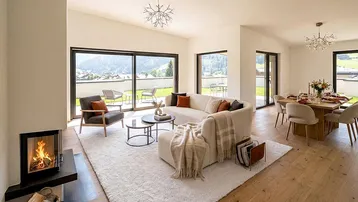 Heller, offener Wohn- und Essbereich mit Kamin, Holzboden und Zugang zur Terrasse mit Bergblick.