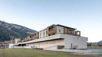 Modernes Mehrfamilienhaus mit Balkonen, Photovoltaikanlage und Bergblick in ländlicher Umgebung.