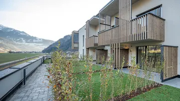 Moderne Wohnanlage mit Balkonen und kleinen Grünflächen vor einer beeindruckenden Bergkulisse.