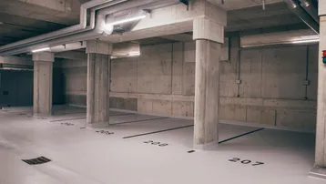 Moderne Tiefgarage mit nummerierten Stellplätzen, Betonwänden und sichtbaren Installationen an der Decke.