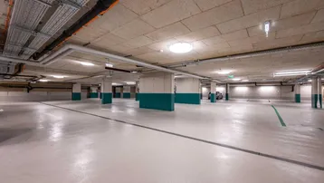 Helle und saubere Tiefgarage mit Betonboden und sichtbaren Installationen an der Decke.