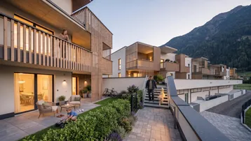 Moderne Wohnanlage mit Terrassen, Balkonen und Blick auf die umliegende Berglandschaft bei Sonnenuntergang.