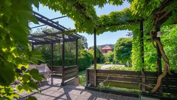 Überdachte Terrasse unter einer begrünten Pergola mit Gartenmöbeln und Weitblick.