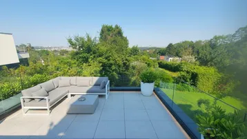 Geräumige Dachterrasse mit modernen Loungemöbeln, Glasgeländer und weitem Blick ins Grüne und auf die Stadt.