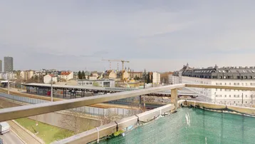 Blick über die Stadt mit einem Bahnhof und Gebäuden im Hintergrund unter bewölktem Himmel.