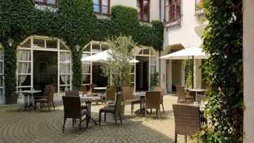 Gemütlicher Innenhof mit Tischen, Stühlen und Sonnenschirmen, umgeben von einer mit Efeu bewachsenen Fassade.
