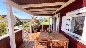 Überdachte Holzterrasse mit Esstisch und Stühlen, ideal für Mahlzeiten im Freien mit Blick ins Grüne.