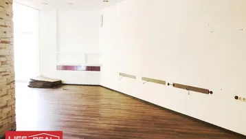 Heller, leerer Geschäftsraum mit modernem Laminatboden und einer Wandverkleidung aus Stein.