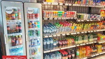 Ein gut gefüllter Gang in einem Supermarkt oder Geschäft mit einer großen Auswahl an Getränken in Regalen und Kühlern.