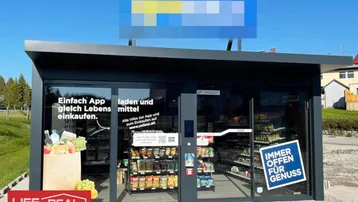 Modernes, kleines Ladenlokal mit großen Glasfronten und Selbstbedienungsangebot, umgeben von Grünflächen.