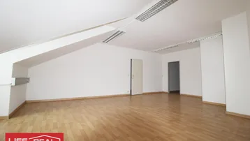 Geräumiger, leerer Dachraum mit schrägen Wänden, Laminatboden und Deckenleuchten, bereit zur individuellen Gestaltung.