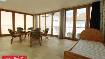 Lichtdurchfluteter Wintergarten mit Rattan-Sitzgruppe, Einzelbett und Zugang zu einem französischen Balkon.