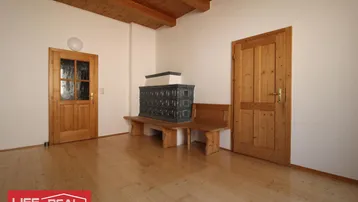 Geräumiger Innenraum mit traditionellem Kachelofen, Holzbalkendecke und hellem Holzfußboden.