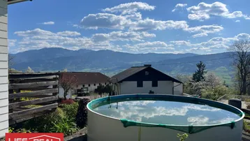 Außenbereich mit einem Aufstellpool und weitem Blick auf die umliegende Berglandschaft unter blauem Himmel.
