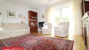 Gemütliches Wohnzimmer mit traditionellem Teppich, bequemen Sesseln und Zugang zum Balkon.