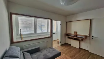 Helles Wohnzimmer mit modernem Sofa, Holzboden und einem Fenster mit Jalousien.