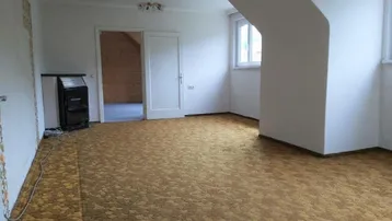 Geräumiges Wohnzimmer mit Teppichboden, Ofenheizung und Dachschräge.