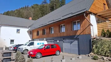 Gebäude mit moderner Holzfassade, grauem Dach und Garagen im Erdgeschoss.
