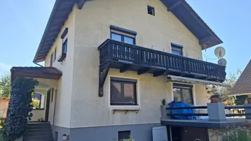 Traditionelles Haus mit Putzfassade, Holzbalkon und Satteldach in sonniger Lage.