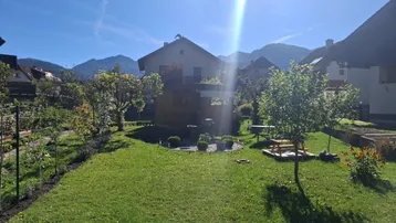 Gepflegter Garten mit Rasenfläche, Obstbäumen und Blick auf die umliegenden Berge.