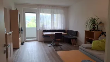 Heller Wohn- und Essbereich mit Laminatboden, gemütlicher Sitzecke und Zugang zum Balkon.