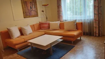 Helles Wohnzimmer mit orangefarbenem Ecksofa, Couchtisch und Parkettboden.