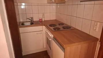 Kleine, funktionale Küche mit Holz-Arbeitsplatte, Spüle und Kochfeld in einfacher Ausführung.