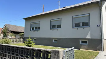 Seitenansicht eines Einfamilienhauses mit Fenstern, Rollläden und einem kleinen Vorgarten.
