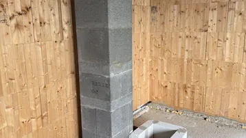 Unfertiger Raum mit Holzwänden, Betonboden und einem gemauerten Kaminfundament.