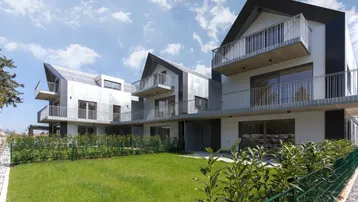 Moderne Reihenhäuser mit Balkonen und gepflegtem Rasenbereich unter blauem Himmel.