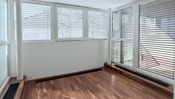 Heller Raum mit vielen Fenstern, Holzfußboden und Jalousien, ideal als Erweiterung des Wohnbereichs.