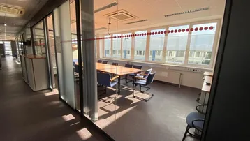 Moderner Büroraum mit Glaswänden, großem Konferenztisch und viel Tageslicht durch die Fensterfront.