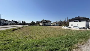 Weitläufiges Grundstück mit grüner Wiese und umliegenden Wohnhäusern unter blauem Himmel.
