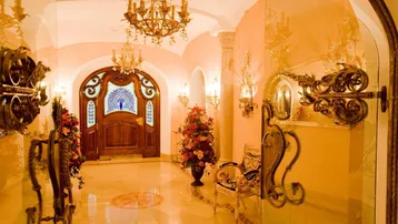 Opulenter Eingangsbereich mit kunstvoller Holztür, glänzendem Marmorboden und eleganten Kronleuchtern.