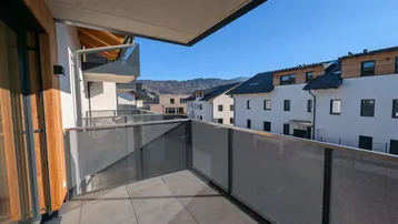 Geräumiger Balkon mit Fliesenboden und Blick auf die umliegende Berglandschaft und Nachbargebäude.