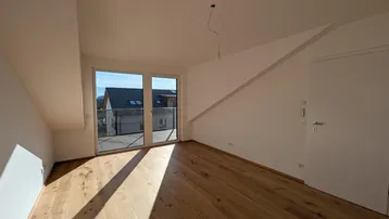 Heller Wohnraum mit Eichenparkett und großem Fenster, das Zugang zu einem französischen Balkon bietet.