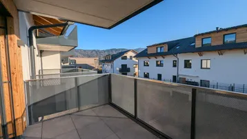 Geräumiger Balkon mit Fliesenboden und Blick auf die umliegende Berglandschaft und Neubauten.