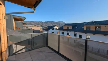 Sonniger Balkon mit Glasgeländer und weitem Blick auf die umliegende Berglandschaft.