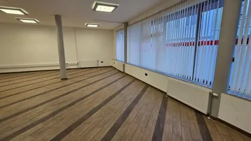 Geräumiger, leerer Büroraum mit großen Fenstern, Jalousien und Holzboden in gutem Zustand.