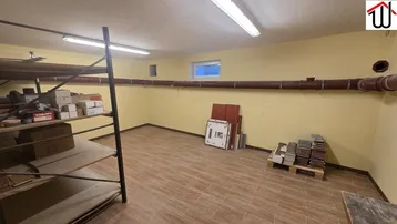 Geräumiger Kellerraum mit gelben Wänden, Fliesenboden, Regalen und einem kleinen Fenster.