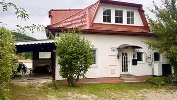 Charmantes Einfamilienhaus mit rotem Dach, weißer Fassade und überdachtem Außenbereich im Grünen.