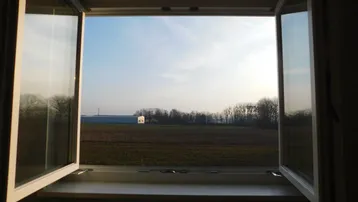 Offenes Fenster mit Blick auf weite Felder und den Horizont unter klarem Himmel.