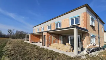 Neubau-Reihenhäuser im Rohbauzustand mit sichtbaren Ziegelwänden und vorbereiteten Terrassenbereichen.