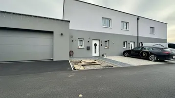 Modernes Reihenhaus mit Garage und gepflasterter Einfahrt unter bewölktem Himmel.