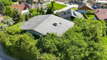 Luftaufnahme eines von Bäumen umgebenen Hauses mit Satteldach in einer Wohngegend.
