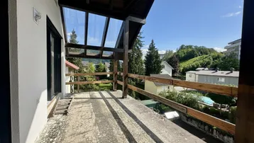 Geräumiger Balkon mit Glasdach und Holzgeländer bietet einen weiten Blick ins Grüne.
