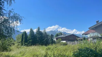 Blick auf ein sonniges Grundstück mit Bergblick und umliegenden Häusern unter blauem Himmel.